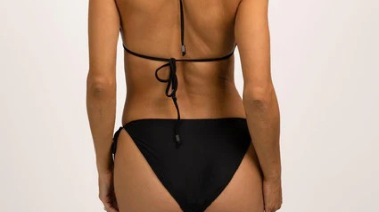 Model wearing Hermosa Tie Bikini Bottom Onyx — sleek black luxury swimwear from Neon Skull designed for confident, minimal style