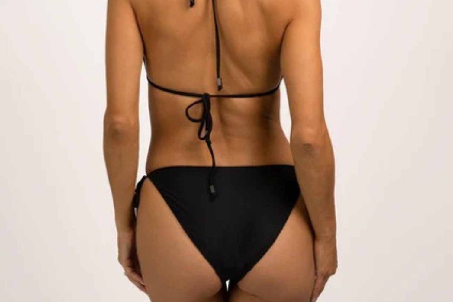 Model wearing Hermosa Tie Bikini Bottom Onyx — sleek black luxury swimwear from Neon Skull with adjustable tie sides