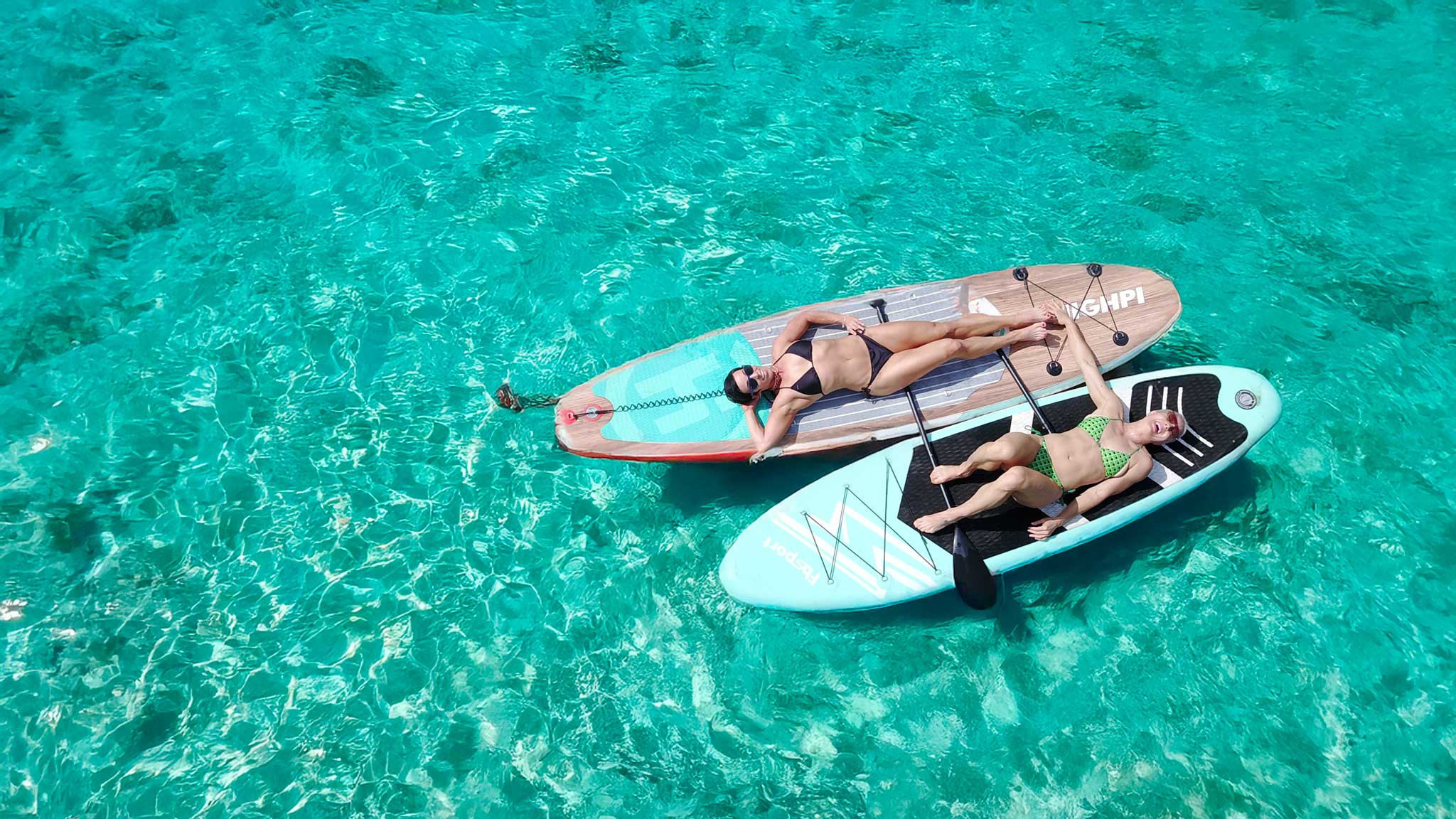 Two people lying on inflatable paddle boards in clear turquoise water